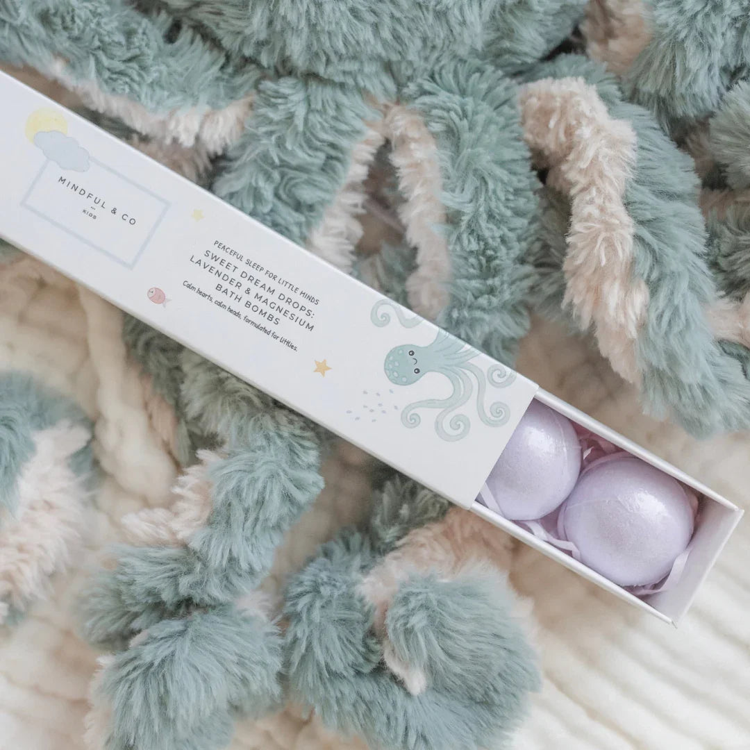 Mindful & Co Kids Lavender & Magnesium Bath Bombs box on plush octopus toy, cozy setting. Come see us at Awaken, Franklin, Tennessee