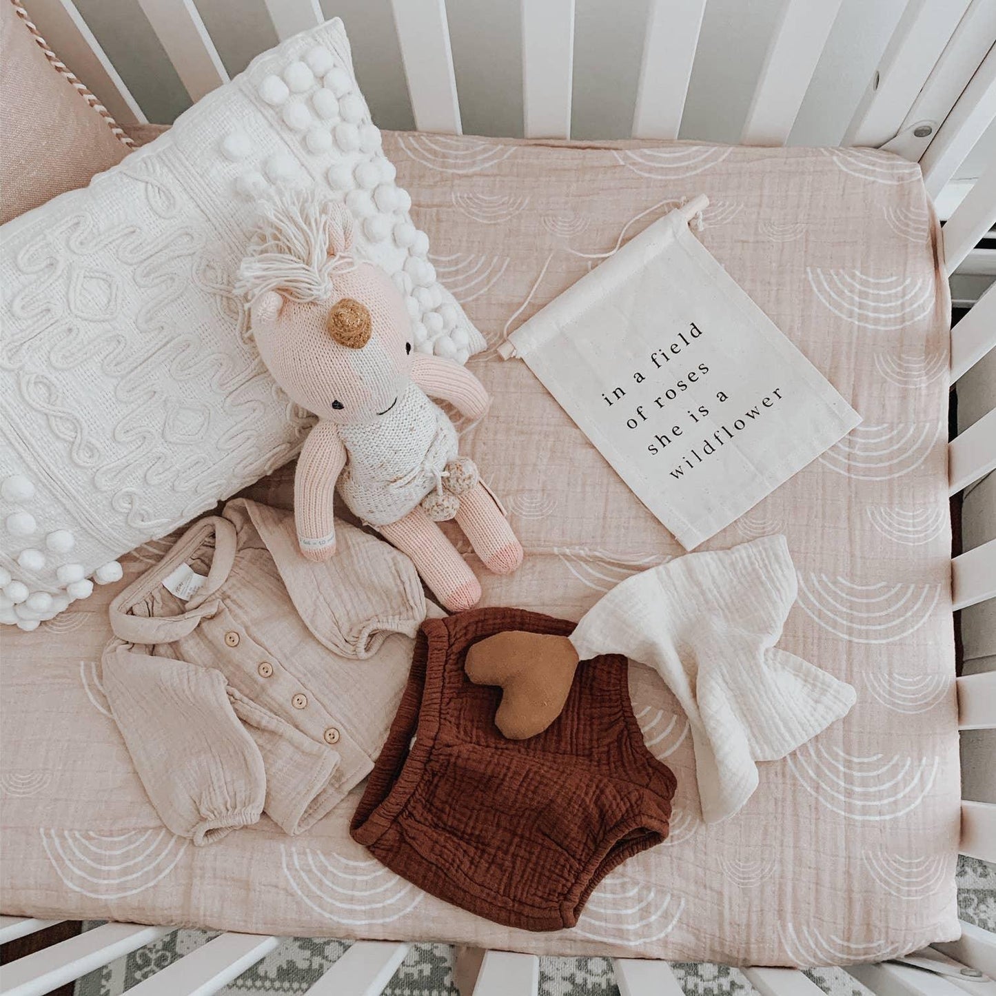 Baby crib with neutral tones, knitted doll, soft pillows, baby clothes and a fabric sign. Come see us at Awaken, Franklin, Tennessee