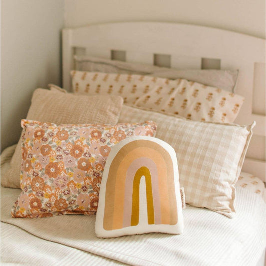 Decorative pillows with floral and rainbow patterns on bed with beige headboard. Come see us at Awaken, Franklin, Tennessee