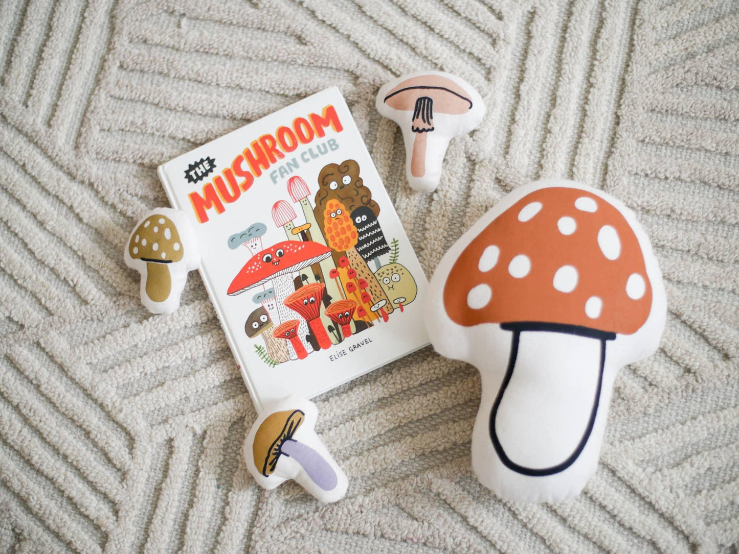 The Mushroom Fan Club book and mushroom plush toys on textured carpet. Come see us at Awaken, Franklin, Tennessee