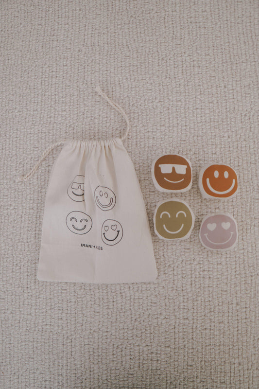 Smile face wooden toys with beige drawstring bag on textured carpet. Come see us at Awaken, Franklin, Tennessee
