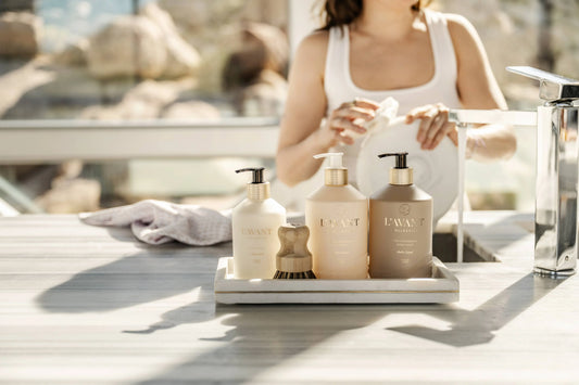 L'AVANT Collective hand soap and lotion set on countertop with woman washing dish in background. Come see us at Awaken, Franklin, Tennessee