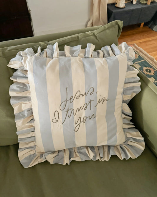 Blue and white striped decorative pillow with ruffles and 'Jesus, I trust in you' text on green sofa. Come see us at Awaken, Franklin, Tennessee