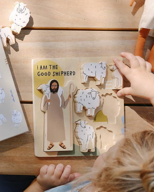 Child playing with wooden Good Shepherd puzzle featuring Jesus and sheep on a wooden table. Come see us at Awaken, Franklin, Tennessee