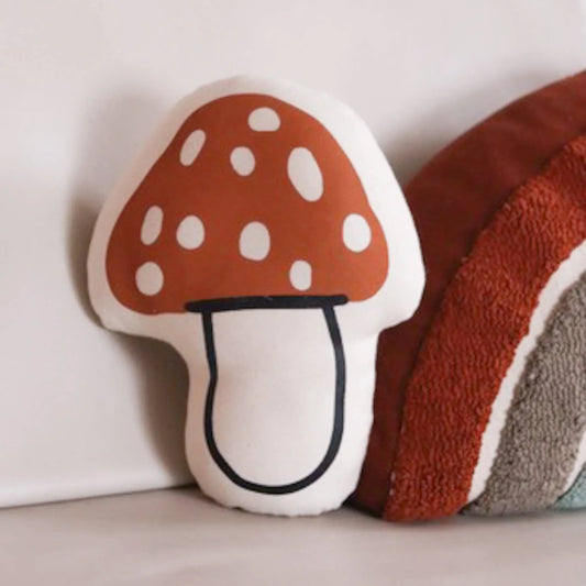 Red and white spotted mushroom pillow next to textured rainbow cushion on grey surface. Come see us at Awaken, Franklin, Tennessee