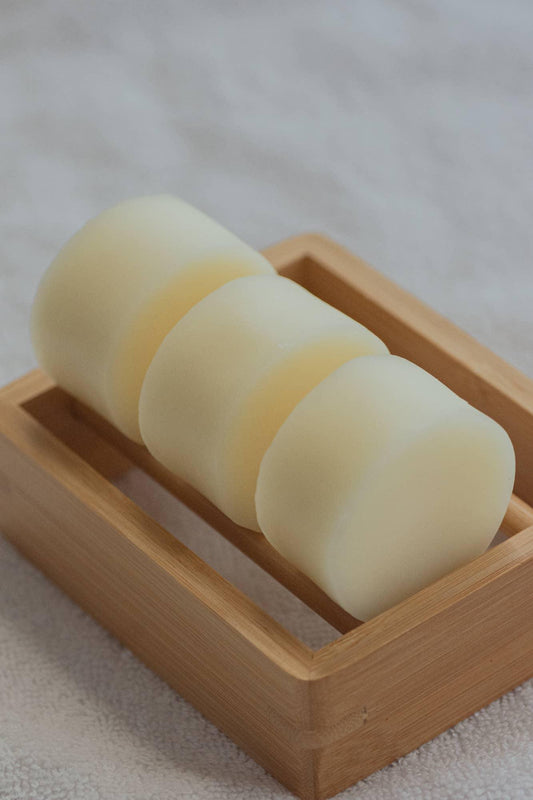 Three round white soap bars in a wooden dish on a textured cloth, Come see us at Awaken, Franklin, Tennessee
