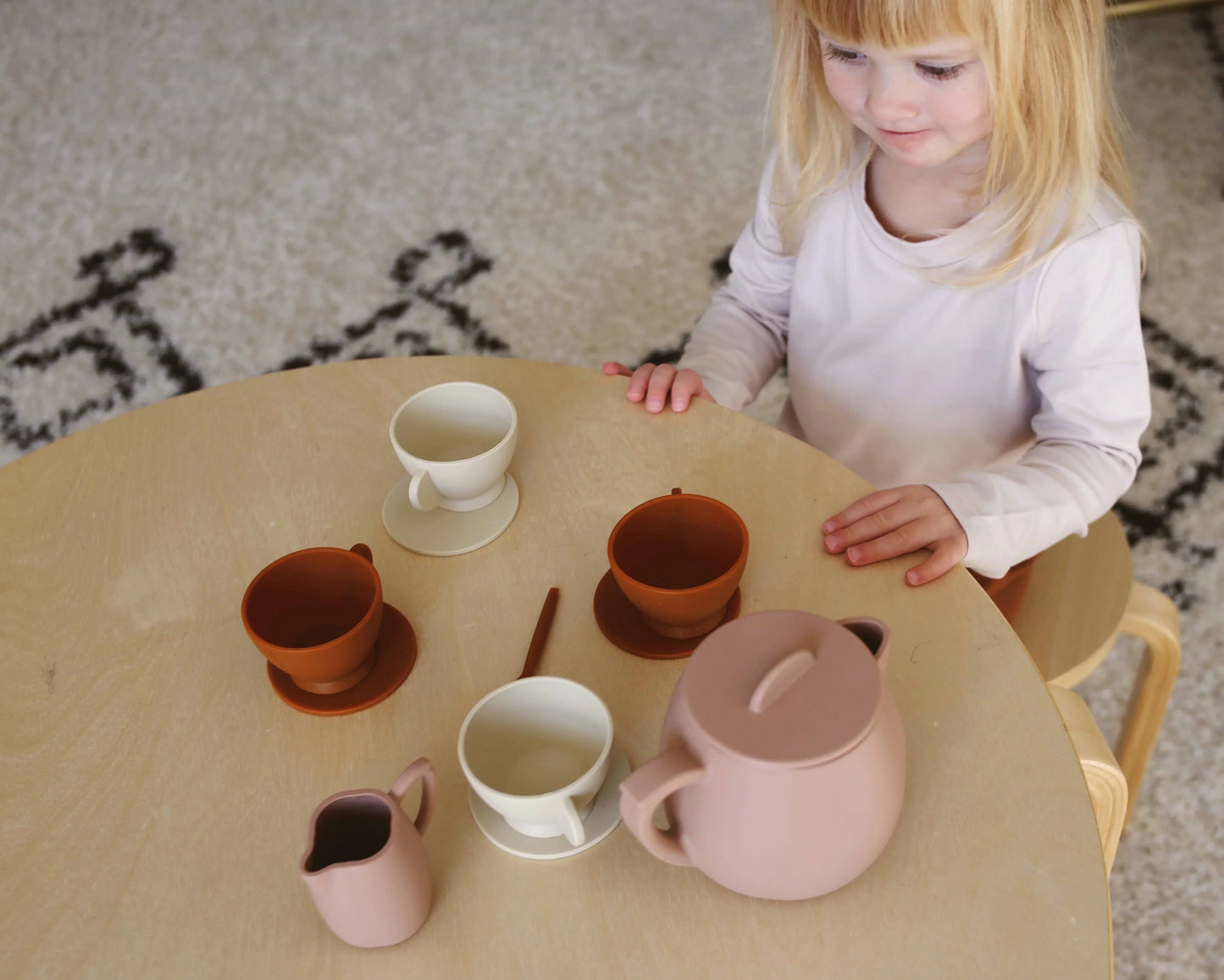 Child playing with pastel tea set on round wooden table, cozy rug background. Come see us at Awaken, Franklin, Tennessee