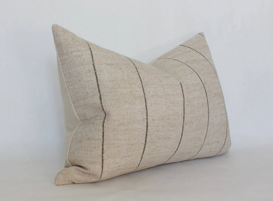 Beige lumbar pillow with black vertical stripes on white background. Come see us at Awaken, Franklin, Tennessee