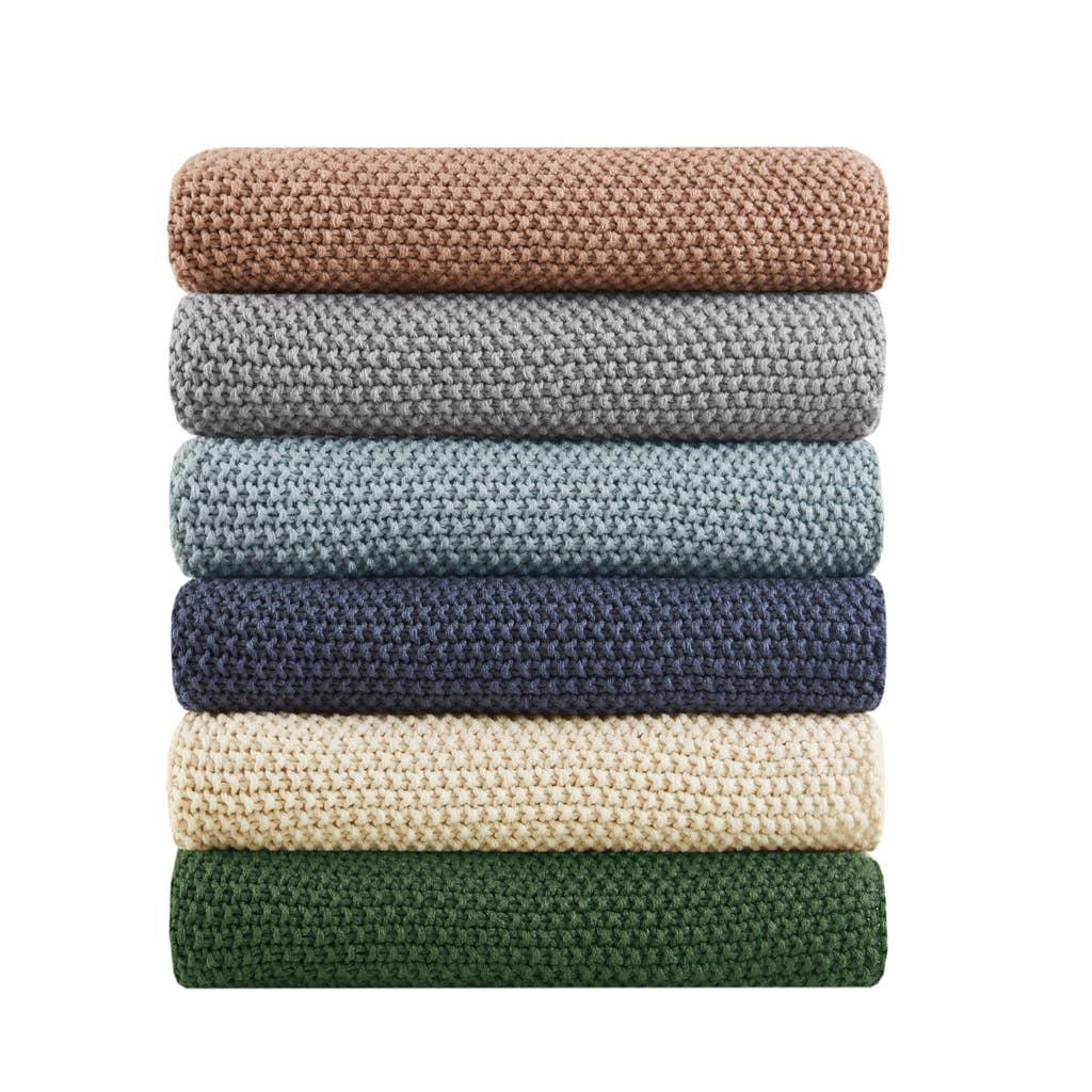 Stack of six knitted blankets in brown, gray, blue, navy, cream, and green colors. Come see us at Awaken, Franklin, Tennessee