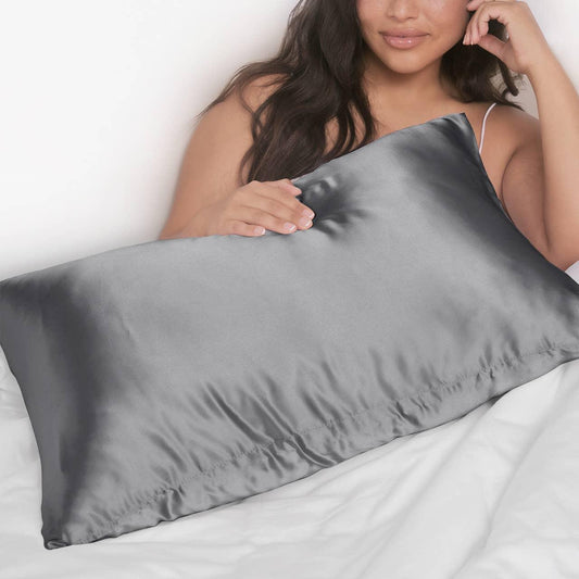 Woman holding smooth gray satin pillow on white bedding for skincare comfort. Come see us at Awaken, Franklin, Tennessee