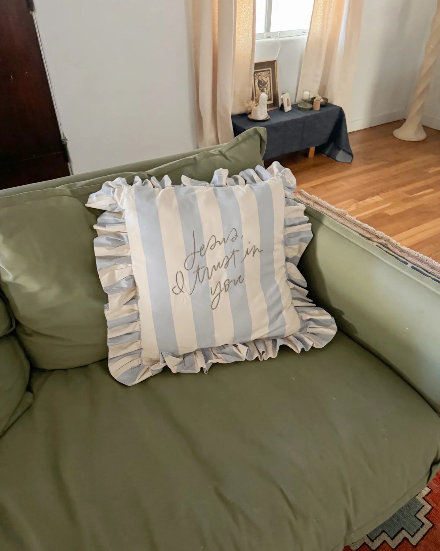 Blue and white striped ruffled pillow with Jesus I trust in you text on green couch in living room Come see us at Awaken, Franklin, Tennessee