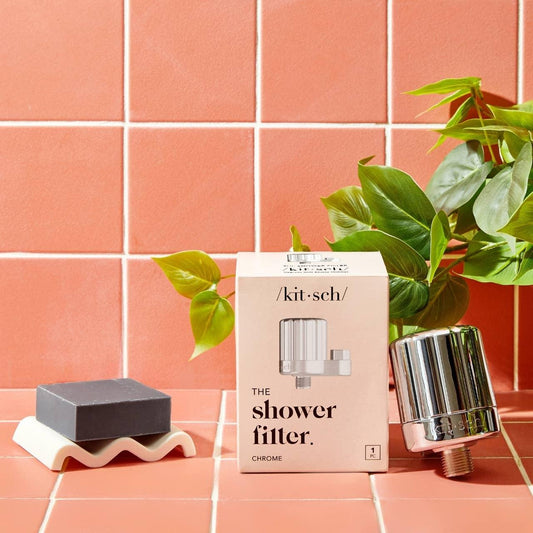 Kitsch shower filter, box, black soap, and plant on pink tile. Come see us at Awaken, Franklin, Tennessee.