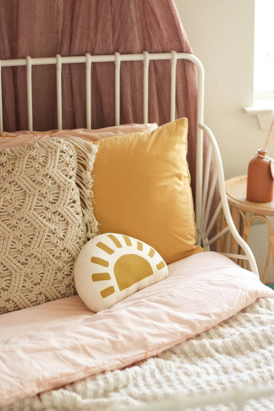 Cozy bed with macrame pillow, yellow cushion, sun print pillow, soft pink bedding. Come see us at Awaken, Franklin, Tennessee