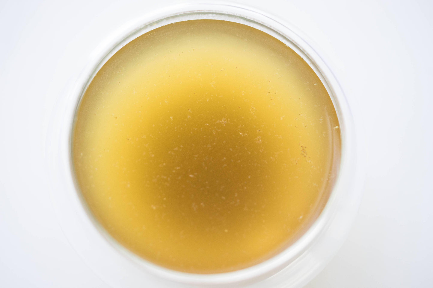 Close-up of translucent golden wax balm in a clear round container, Come see us at Awaken, Franklin, Tennessee