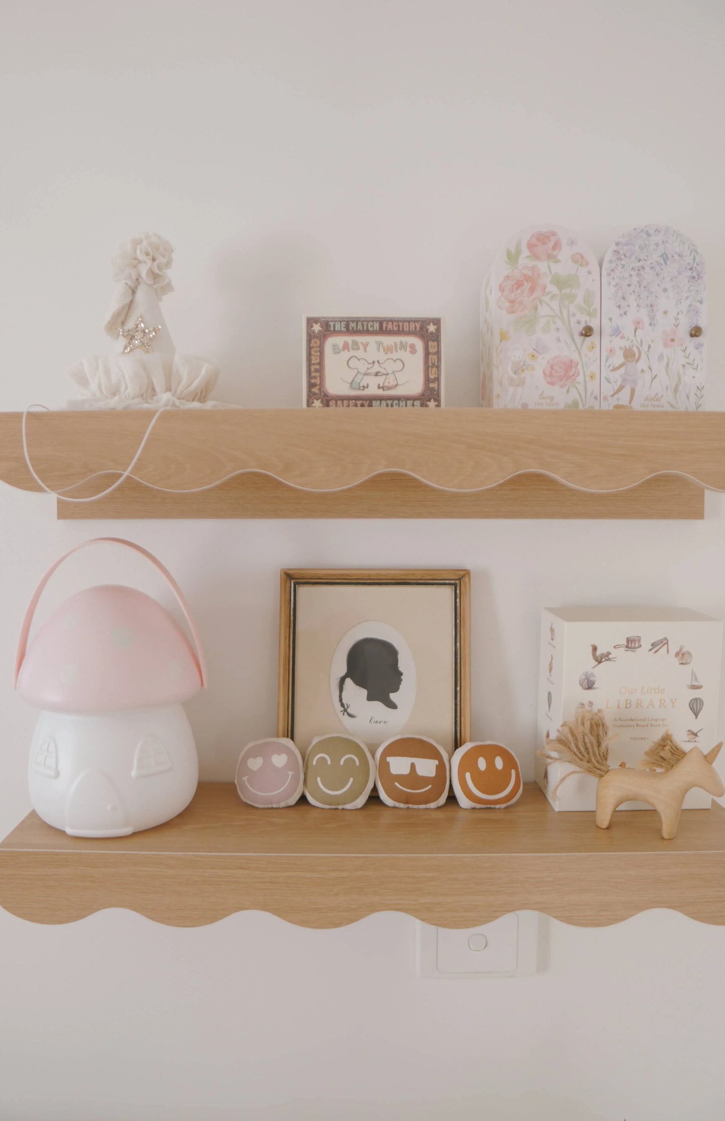 Decorative wooden shelves with kids' books, toys, smiley face cushions, and a framed silhouette art. Come see us at Awaken, Franklin, Tennessee