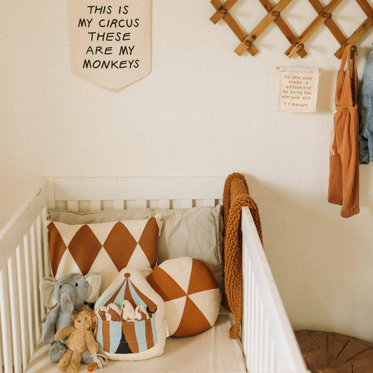 Minimalist white baby crib with brown and cream circus-themed pillows, stuffed animals, and wall banners. Come see us at Awaken, Franklin, Tennessee