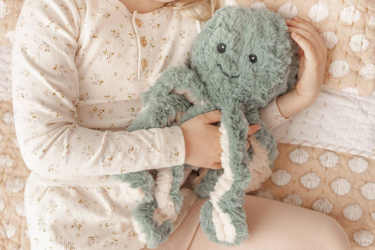 Child in floral pajamas hugging a soft green plush octopus on a seashell quilt Come see us at Awaken, Franklin, Tennessee
