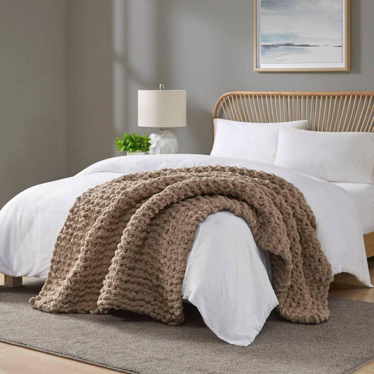 Cozy bedroom with white bedding, chunky beige knitted throw on bed, rattan headboard, lamp, and wall art. Come see us at Awaken, Franklin, Tennessee