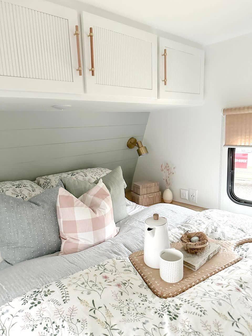 Cozy bedroom with floral bedding, plaid pillow, wooden tray, and brass reading light. Come see us at Awaken, Franklin, Tennessee