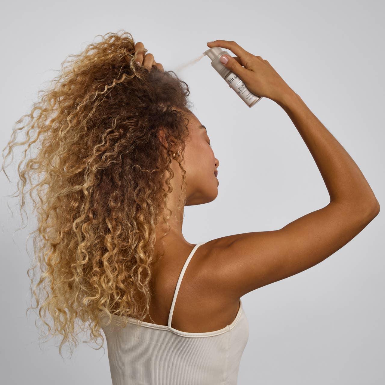 Woman with curly hair using hair product spray, Come see us at Awaken, Franklin, Tennessee.