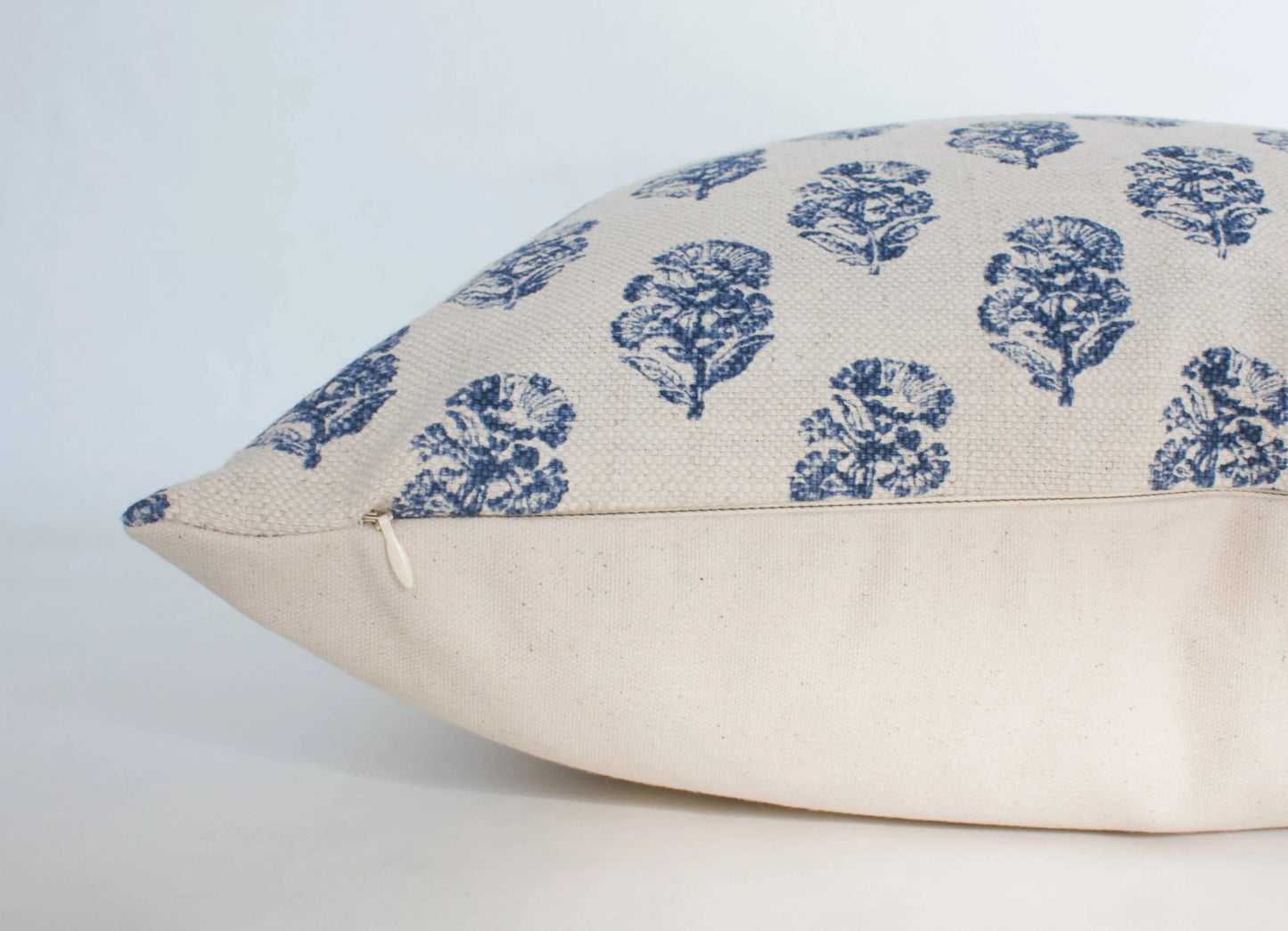 Beige linen pillow with blue floral prints and zipper detail on white background. Come see us at Awaken, Franklin, Tennessee