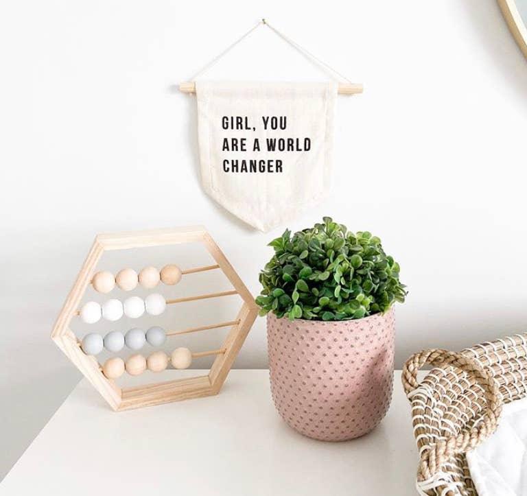 Decorative wooden abacus, pink dotted pot with green plant, and banner saying 'Girl, you are a world changer' Come see us at Awaken, Franklin, Tennessee