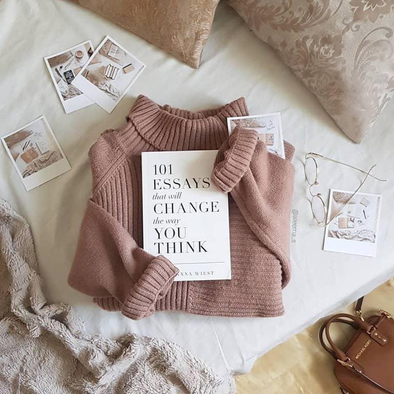 Mauve turtleneck sweater with book 101 Essays That Will Change The Way You Think on bed with decor photos and glasses, Come see us at Awaken, Franklin, Tennessee