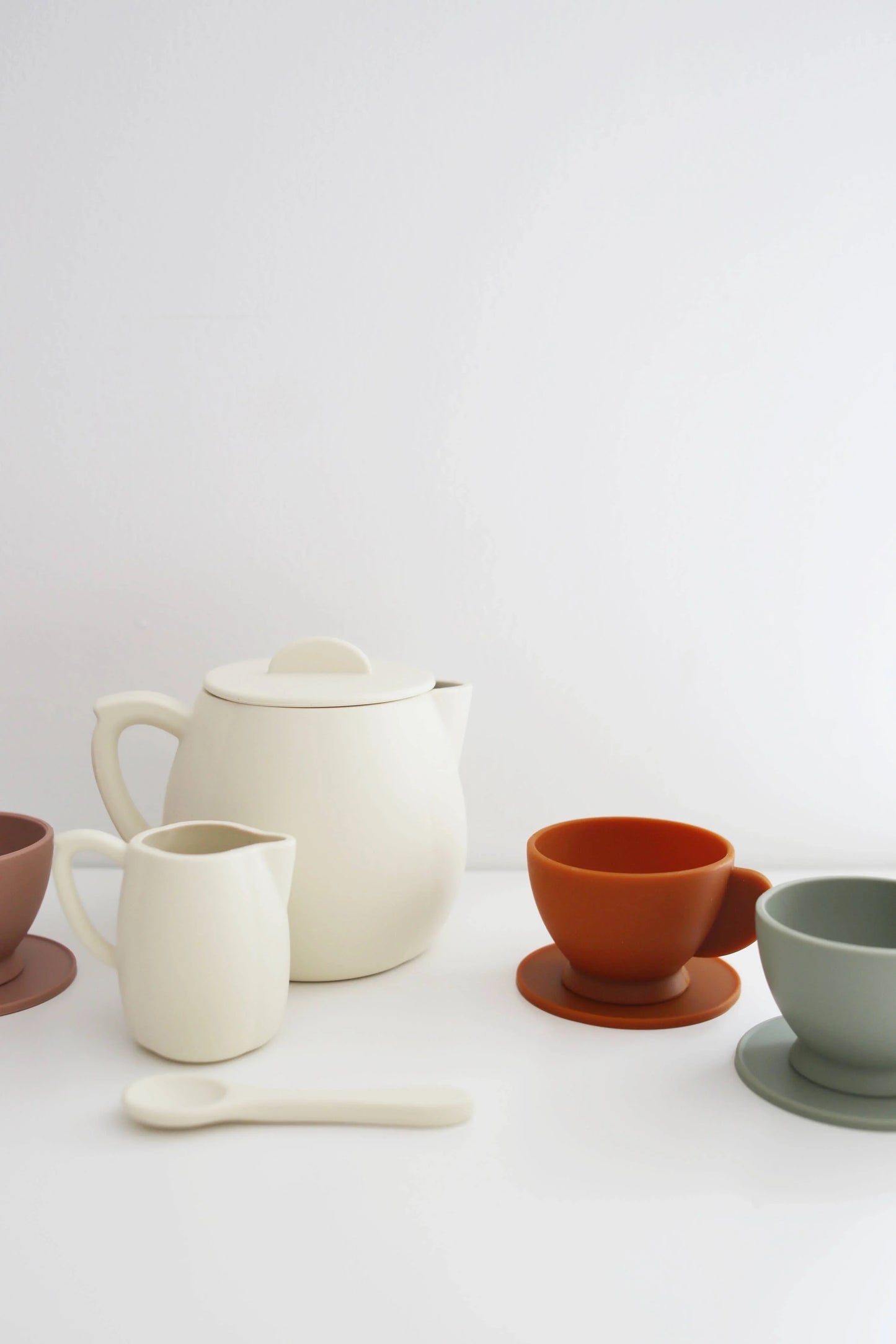 Minimalist ceramic teapot, creamer, spoon, and colorful cups on white surface. Come see us at Awaken, Franklin, Tennessee