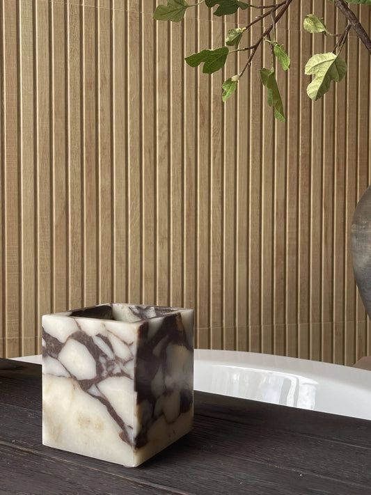 Marble square container on dark wood table with vertical wood panel wall and green plant branch. Come see us at Awaken, Franklin, Tennessee