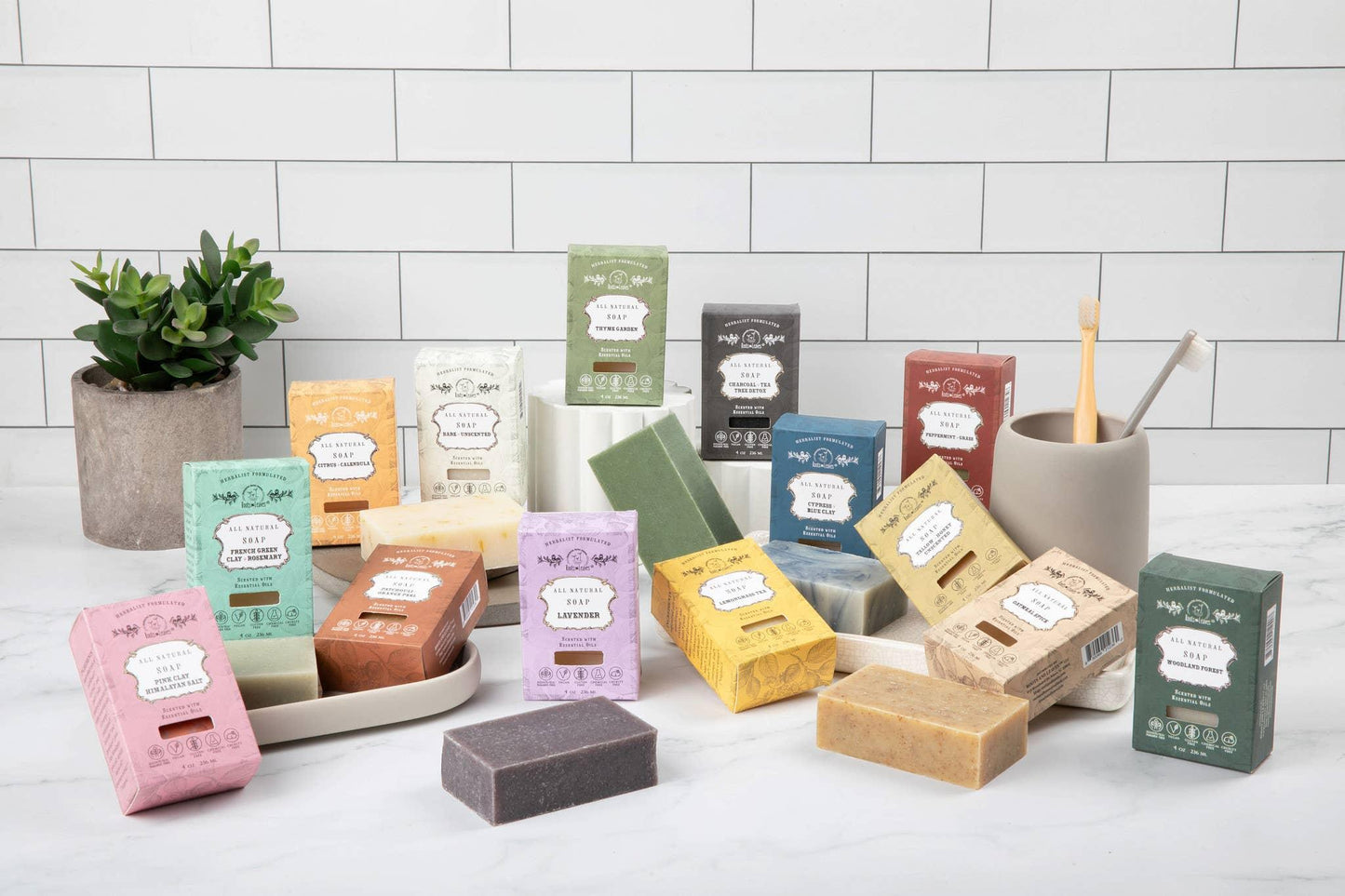 Various colorful all-natural soap bars with essential oils displayed on white marble with plant and toothbrush holder. Come see us at Awaken, Franklin, Tennessee
