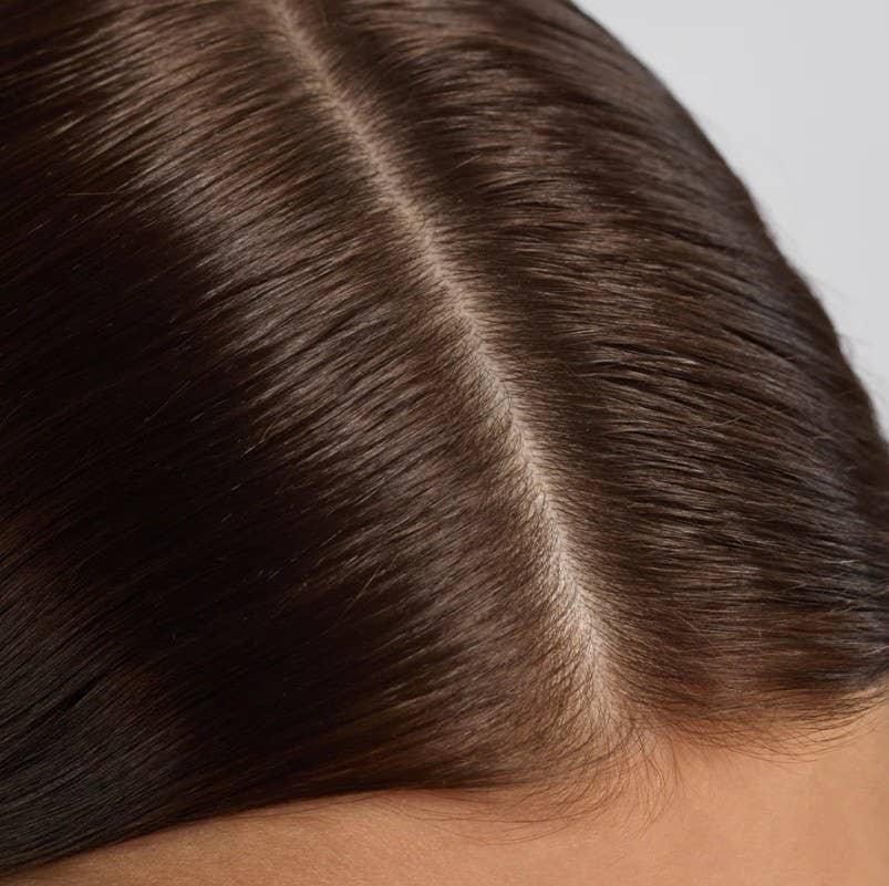 Close-up of smooth, shiny brown hair with a middle part on a light background. Come see us at Awaken, Franklin, Tennessee