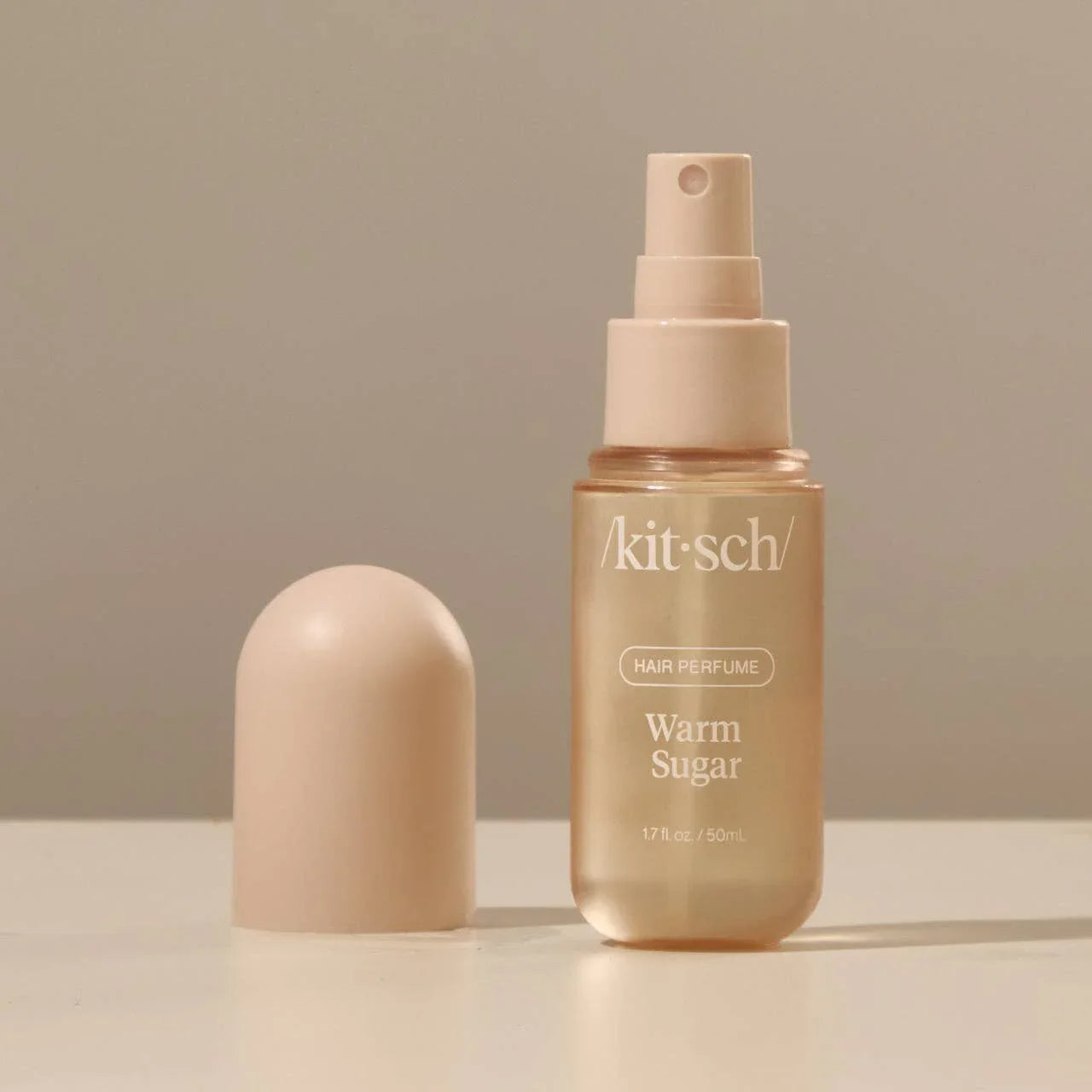 Kitsch Warm Sugar hair perfume spray bottle with beige cap on neutral background. Come see us at Awaken, Franklin, Tennessee