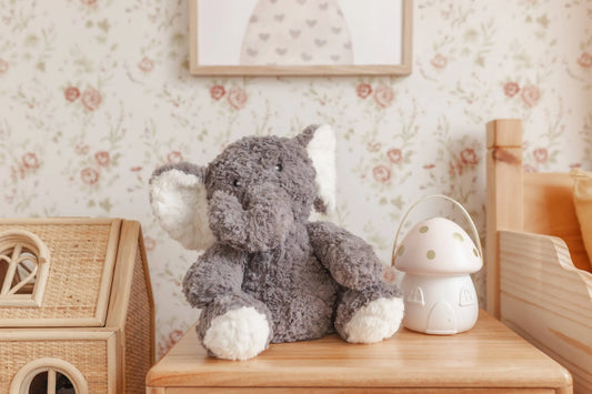 Plush gray elephant toy and mushroom night light on wooden table in floral nursery. Come see us at Awaken, Franklin, Tennessee