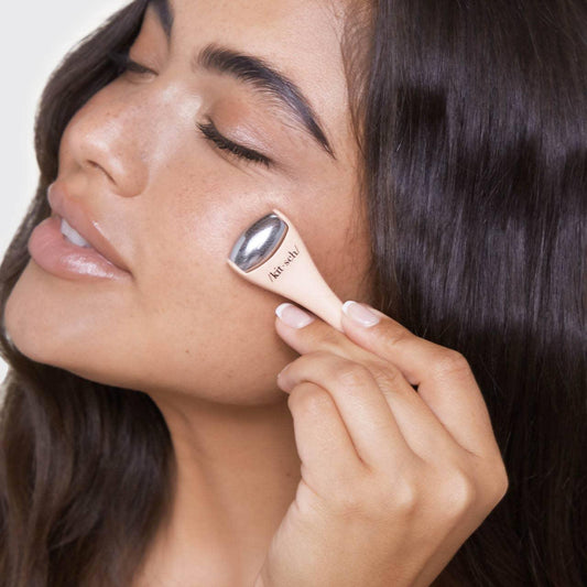 Woman using Kitsch facial massage tool on cheek with closed eyes, smooth skin, dark hair. Come see us at Awaken, Franklin, Tennessee