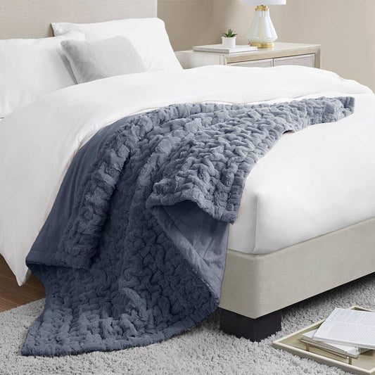 Cozy gray textured throw blanket on white bed in modern bedroom with nightstand, lamp, and books. Come see us at Awaken, Franklin, Tennessee