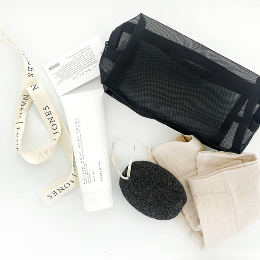 Nashi Jones body creme, black mesh toiletry bag, pumice stone, and beige cloths on white surface. Come see us at Awaken, Franklin, Tennessee