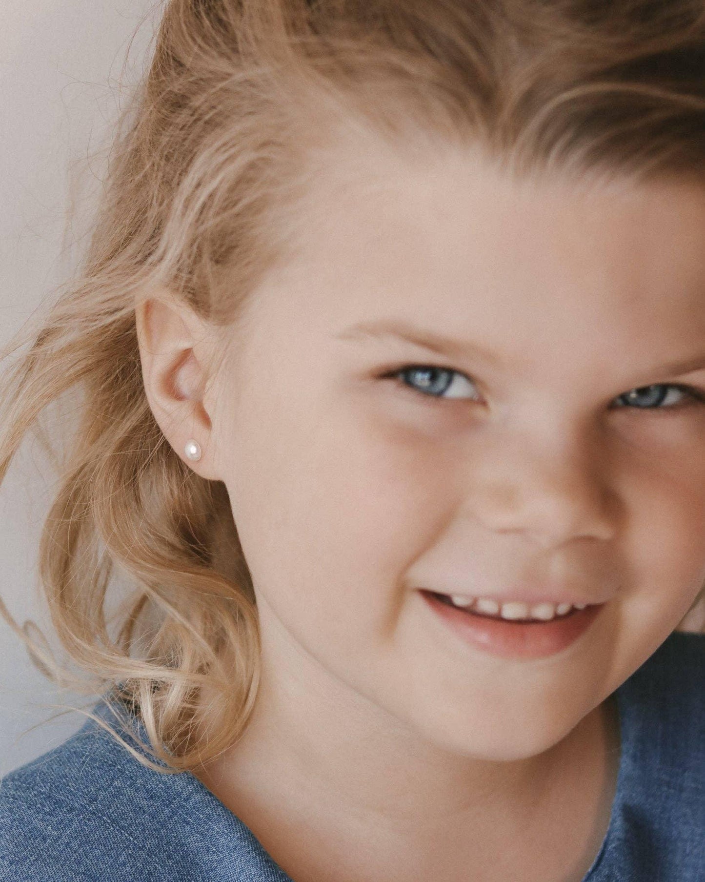 Smiling young girl with blonde hair and pearl earrings wearing blue top. Come see us at Awaken, Franklin, Tennessee