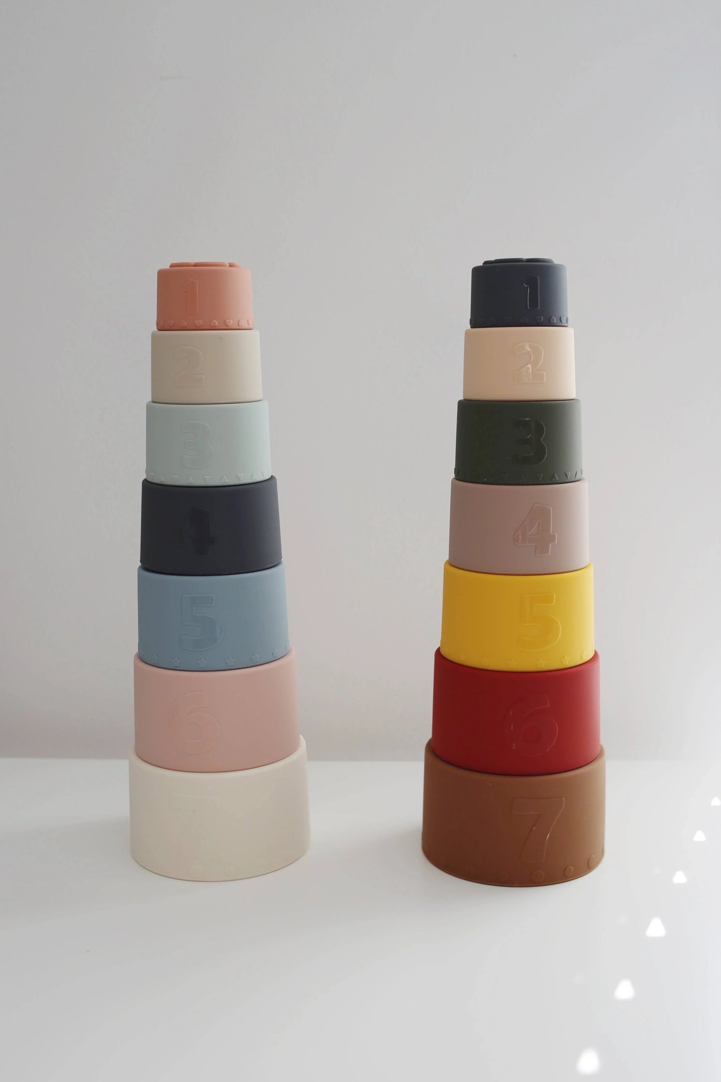 Two stacks of colorful numbered silicone stacking cups on white surface with gray background. Come see us at Awaken, Franklin, Tennessee