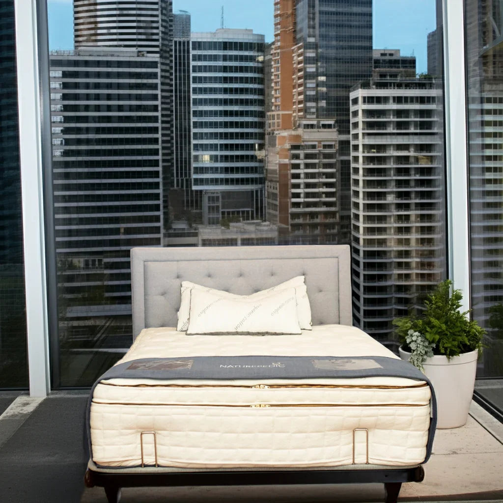 Modern bedroom with natural mattress and gray upholstered bed, city skyline view, plants, Come see us at Awaken, Franklin, Tennessee
