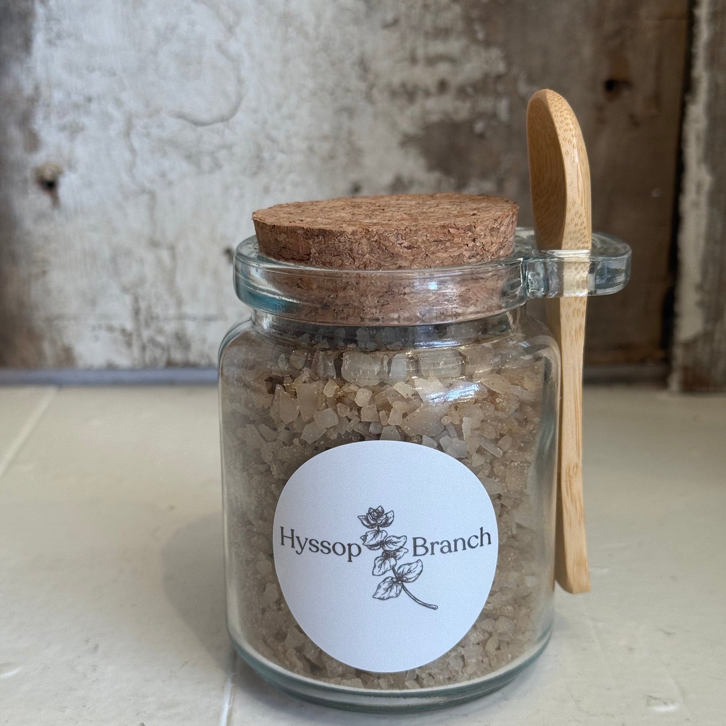 Glass jar of brown bath salt with wooden spoon, Hyssop Branch label, rustic background. Come see us at Awaken, Franklin, Tennessee