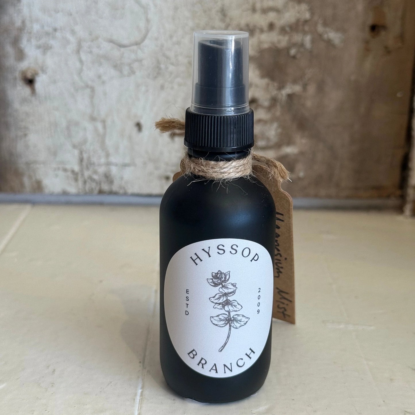 Matte black Hyssop Branch spray bottle with botanical label and twine, on rustic surface. Come see us at Awaken, Franklin, Tennessee