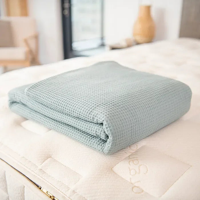 Folded light blue waffle weave blanket on bed, cozy bedding. Come see us at Awaken, Franklin, Tennessee.