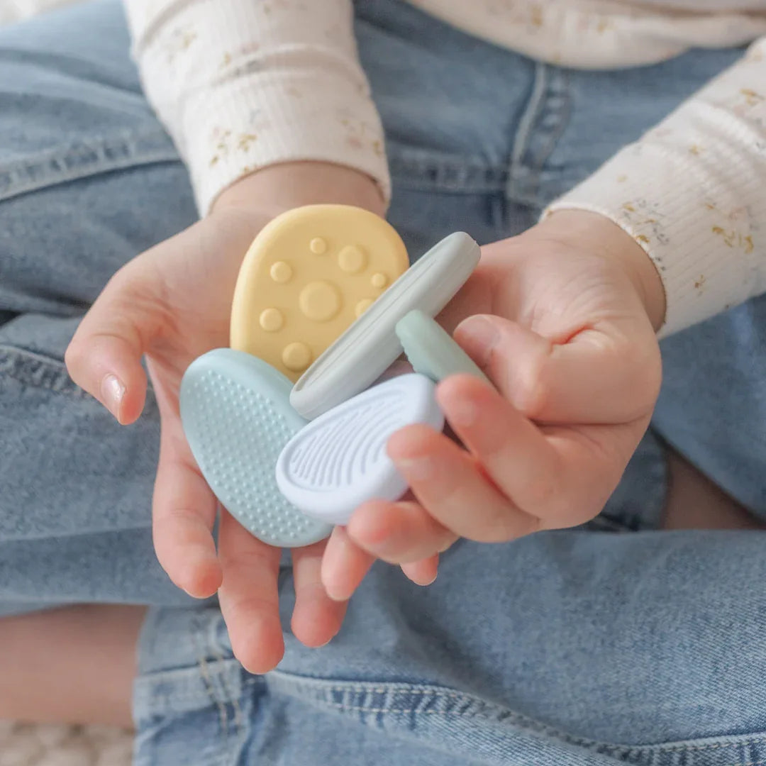 Child holding colorful textured sensory teething toys sitting cross-legged in jeans Come see us at Awaken, Franklin, Tennessee