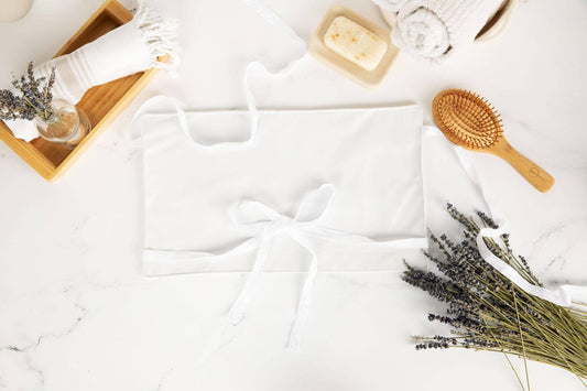 White apron surrounded by lavender, wooden tray with towel, rolled towels, soap, and wooden hairbrush. Come see us at Awaken, Franklin, Tennessee