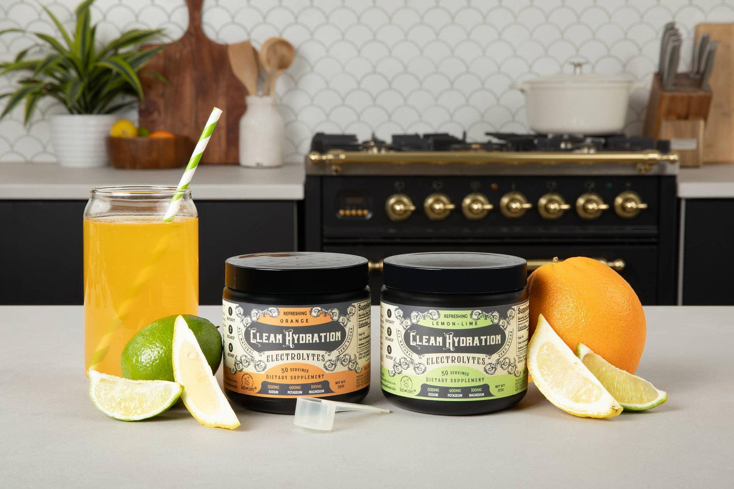 Two Clean Hydration electrolyte supplement containers with orange and lemon-lime flavors, fresh citrus fruits, and a glass of juice on kitchen counter. Come see us at Awaken, Franklin, Tennessee