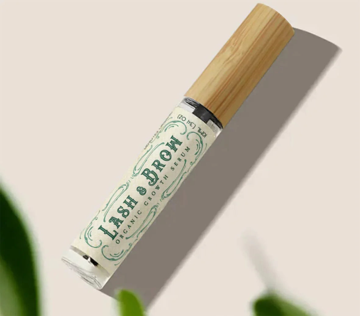 Lash & Brow organic growth serum with bamboo cap on beige background and green leaf, Come see us at Awaken, Franklin, Tennessee