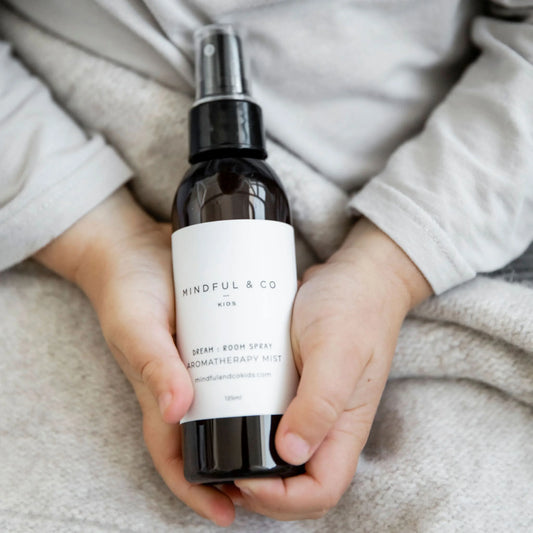 Child holding Mindful & Co Kids Dream Room Spray aromatherapy mist bottle, soft fabric background. Come see us at Awaken, Franklin, Tennessee