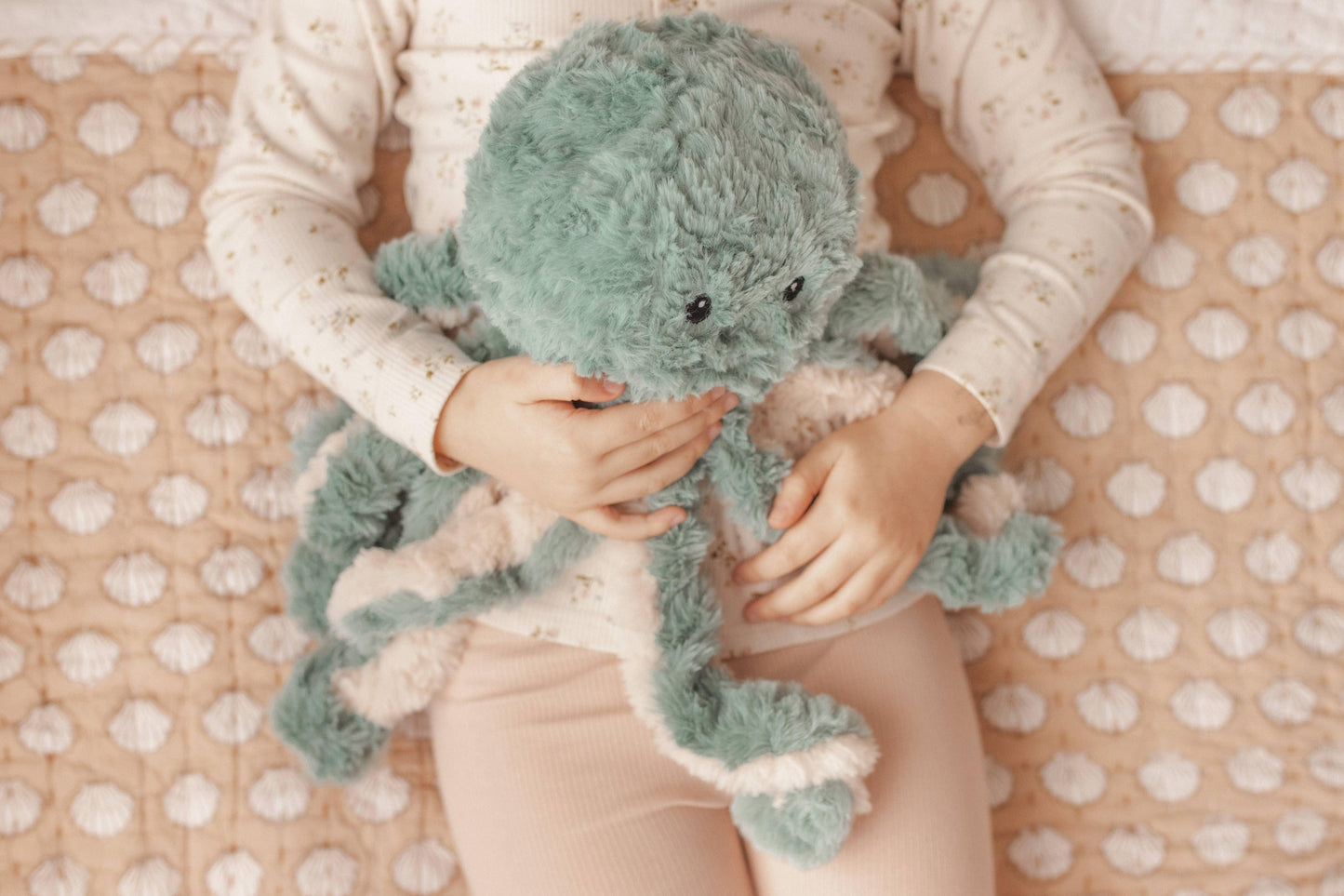 Child holding a soft plush octopus toy on a textured pink blanket, cozy children's room. Come see us at Awaken, Franklin, Tennessee