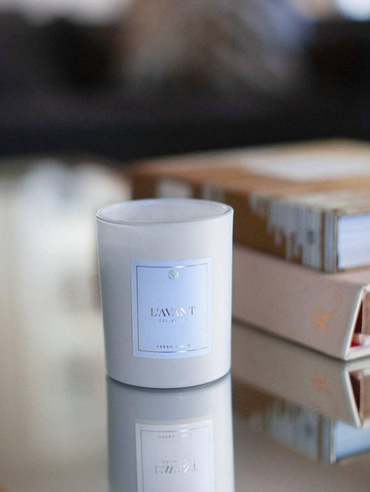 L'AVANT Collective Fresh Linen candle on glass table, books in background, Come see us at Awaken, Franklin, Tennessee