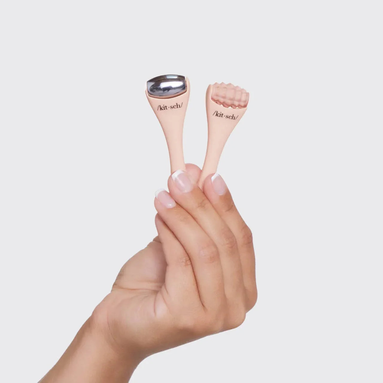 Hand holding two pink facial massage tools with metal and textured heads, branded kitsch, white background. Come see us at Awaken, Franklin, Tennessee